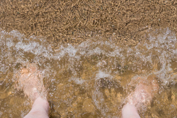 Men's feet in the water at the sandy shore