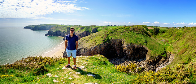 Single Hispanic man lifestyle portrait at beach standing on headland at Skrinkle Haven on the Pembrokeshire Coast