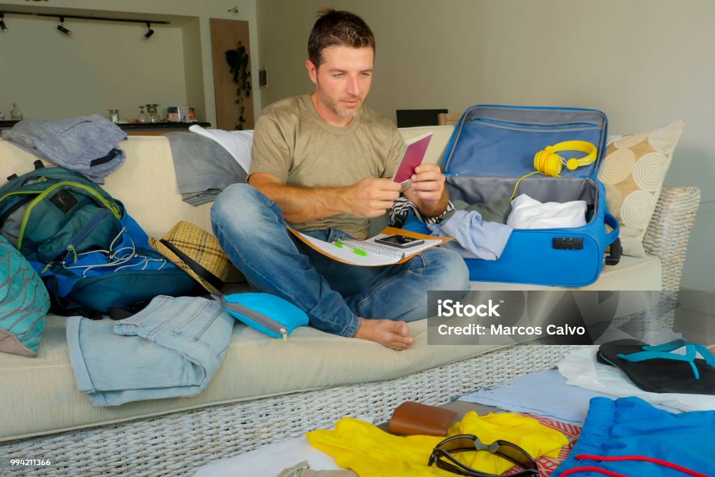 young attractive and happy man holding passport preparing backpack and packing suitcase organizing clothes and things feeling excited and cheerful in summer holidays trip and travel concept 30-39 Years Stock Photo