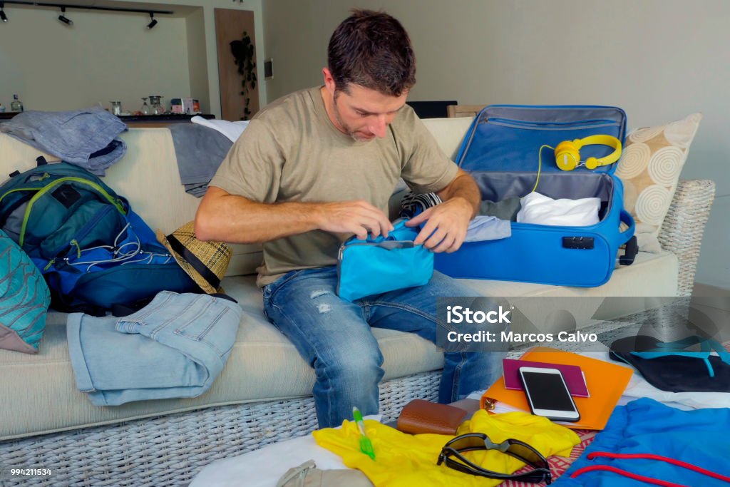 young attractive and happy man at home couch preparing travel back and packing suitcase folding clothes and organizing passport and things before leaving on holidays trip and travel concept Backpack Stock Photo