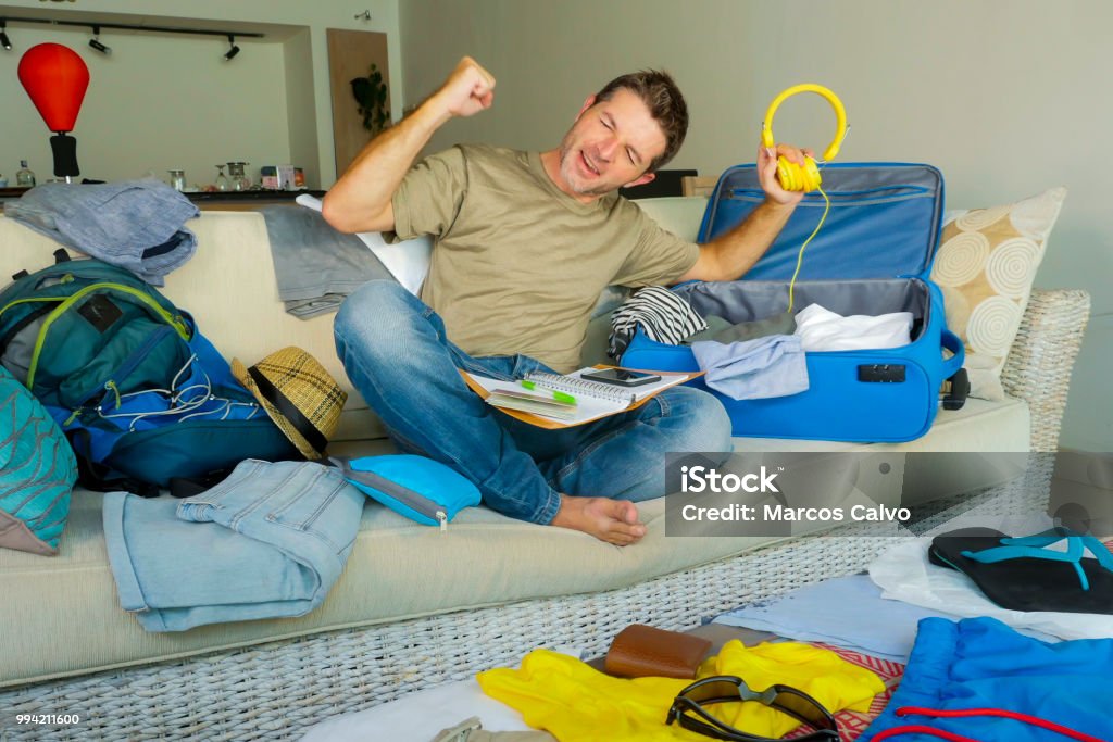 young attractive and happy man at home couch preparing travel back and packing suitcase folding clothes and organizing passport and things before leaving on holidays trip and travel concept 30-39 Years Stock Photo