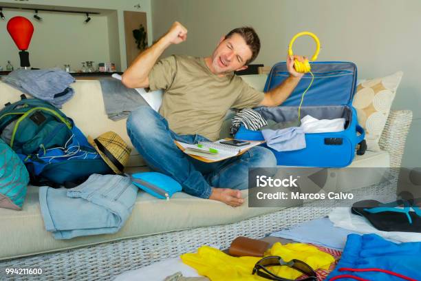 Young Attractive And Happy Man At Home Couch Preparing Travel Back And Packing Suitcase Folding Clothes And Organizing Passport And Things Before Leaving On Holidays Trip And Travel Concept Stock Photo - Download Image Now