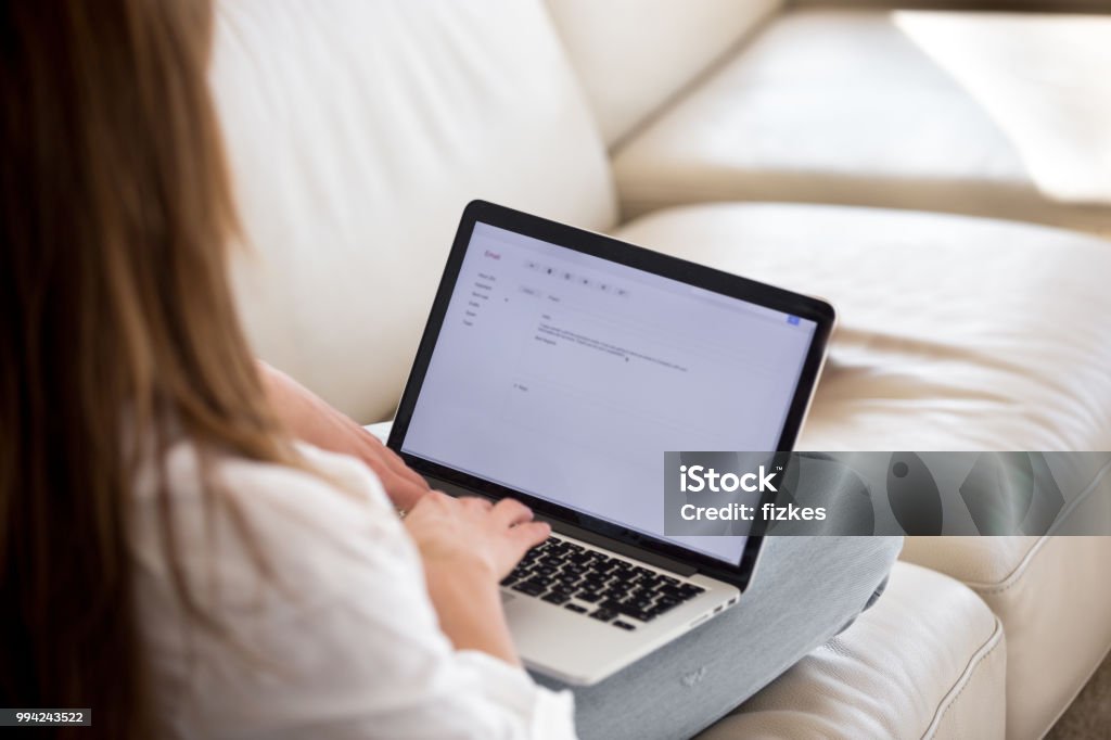 Rear view at woman writing email on laptop at home Rear view at woman writing email on laptop screen online working from home, female applicant typing cover letter applying for job, lady mailing customer support to give feedback or sending request E-Mail Stock Photo
