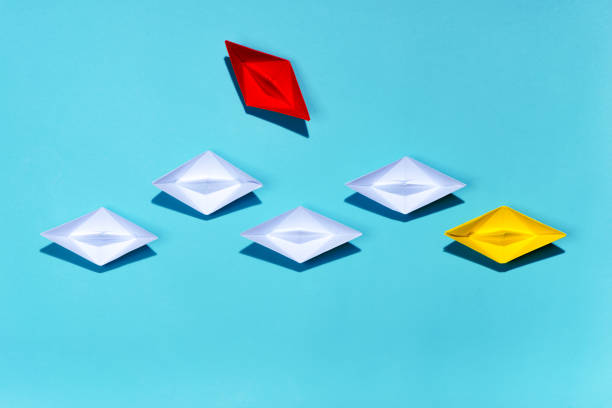 istock Leadership concept. Yellow paper ship leading among white 994254804