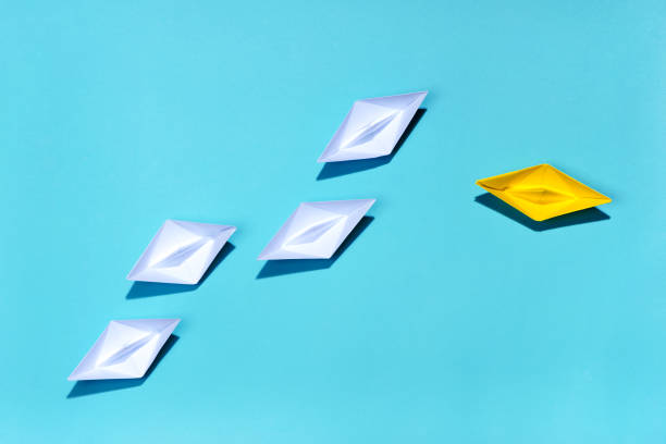 istock Leadership concept. Yellow paper ship leading among white 994254900