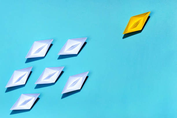 istock Leadership concept. Yellow paper ship leading among white 994255194