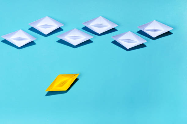 istock Leadership concept. Yellow paper ship leading among white 994255290