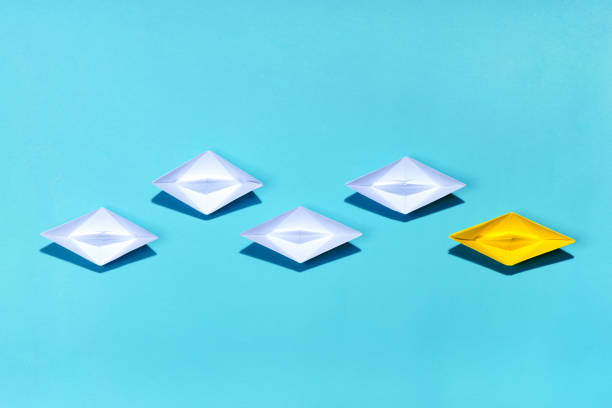 istock Leadership concept. Yellow paper ship leading among white 994255302