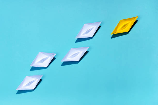 istock Leadership concept. Yellow paper ship leading among white 994257388