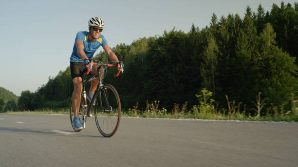 istock LOW ANGLE: Young male biker pedals along empty asphalt road on summer afternoon. 994258452