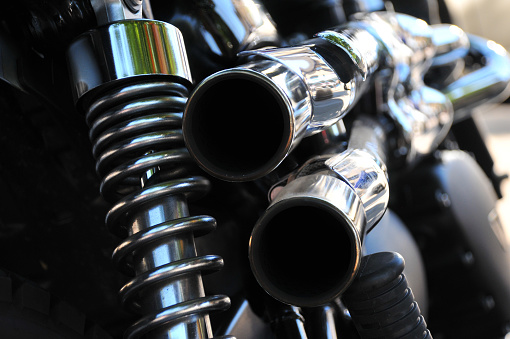 close up abstract rear view of a powerful classic black vintage motorcycle showing suspension and shiny chrome exhaust pipes