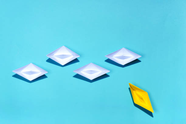 istock Leadership concept. Yellow paper ship leading among white 994258970