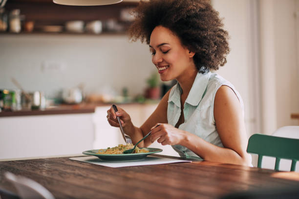 Woman eating pasta. Beautiful mixed race woman eating pasta for dinner while sitting at kitchen table. ADULT EATING stock pictures, royalty-free photos & images