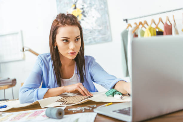 istock serious seamstress looking at laptop at working table 994277758