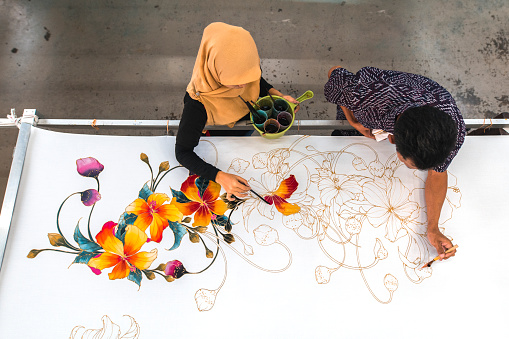 Shot of woman and man coworkers painting in a batik workshop in Kuala Lumpur, Malaysia.
