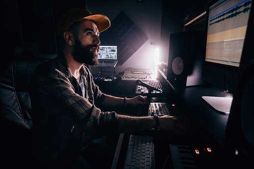 Hipster sound engineer working on audio control panel and producing music in professional music studio