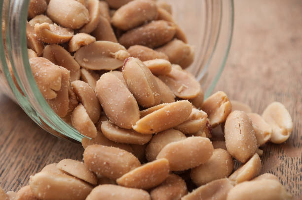 istock salted peanuts falling from glass container on wooden background 994308602