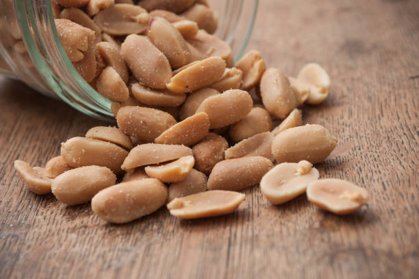 istock salted peanuts falling from glass container on wooden background 994315188