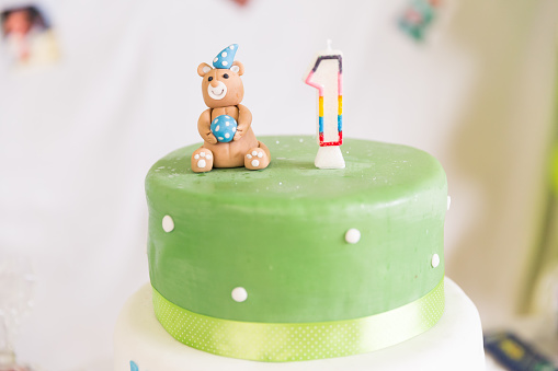 Green and White Birthday Cake with One Year Old Candle and Teddy bear