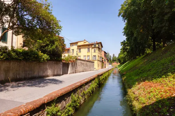Lucca old town cityscape with canal along narrow street and fortified city wall, Tuscany, Italy