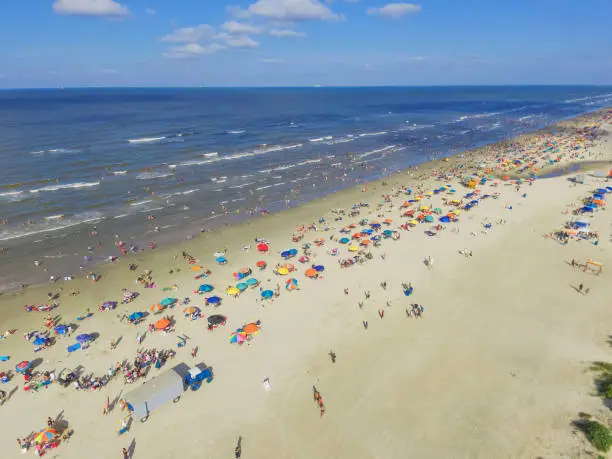 Aerial view beach shoreline on sunny summer day with people bathing, sunbathing, playing volley and relax in Galveston, Texas. Colorful umbrellas, lounge chairs. Holiday maker, summer vacation concept