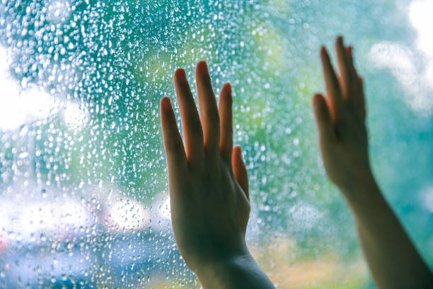 istock Young woman hand touching window on rain day 994366554