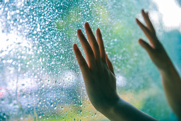 istock Young woman hand touching window on rain day 994366558