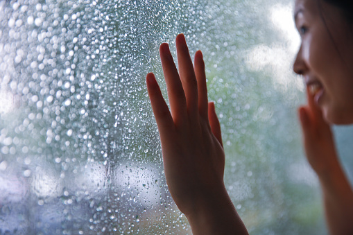 Young woman hand touching window on rain day