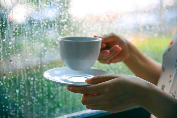 Woman drinking coffee by window on rainy day