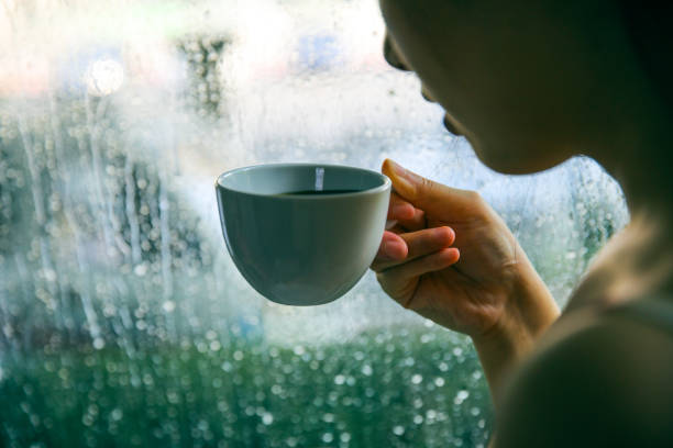 istock Woman drinking coffee by window on rainy day 994367314