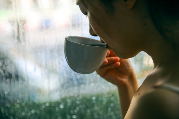 istock Woman drinking coffee by window on rainy day 994367378