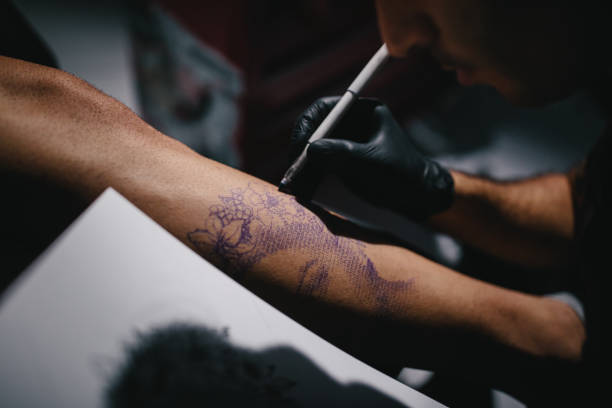 Concentrated tattoo artist transferring and perfecting tattoo design on client's body before tattooing