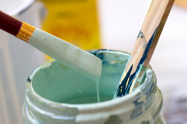 A can of earthtone green paint and brush with an old wooden fence and matching green leaf backgound.