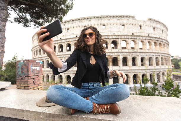 femme assise les jambes croisée et en s’occupant de selfie devant le colisée - international landmark italy amphitheater ancient photos et images de collection