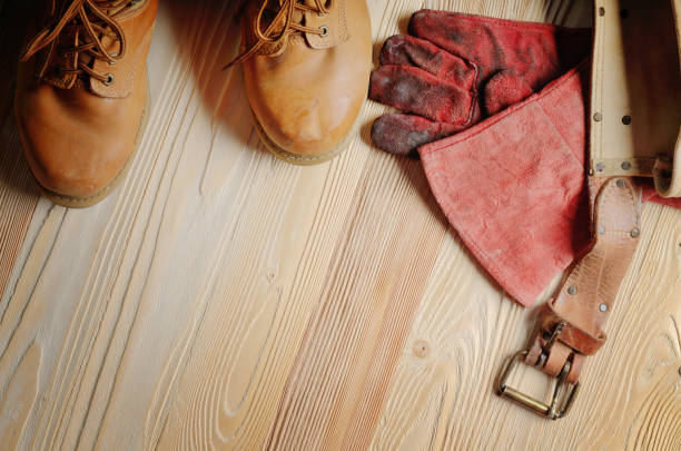 istock Yellow leather used work boots with tool belt and protective gloves on wooden background closeup. Place for text 994403808