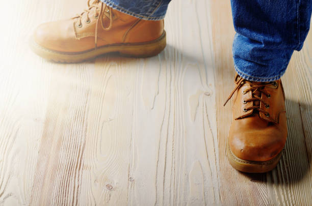 istock Carpenter feet in work boots standing on wooden floor. Place for text 994421882