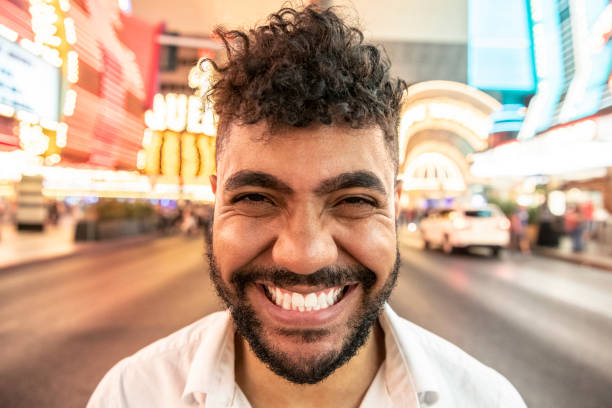 Mixed race man with toothy grin facing camera Closeup portrait of cute mixed race young man, in his 20s with beard and cheerful facial expression, smiling at camera with bright city lights in background wide angle stock pictures, royalty-free photos & images