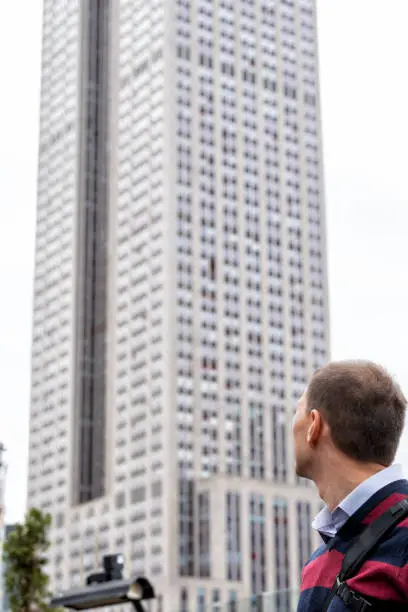 Back of young man standing looking at tall high building skyscraper in urban city in sweater in midtown Manhattan on rooftop in New York City