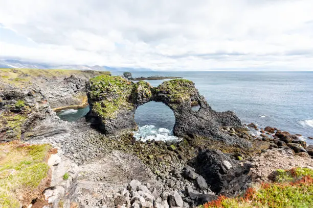 Photo of Landscape view of famous Gatklettur arch rock near Hellnar, National park Snaefellsnes Peninsula, Iceland with rocky ocean sea waves, green grass moss in summer day