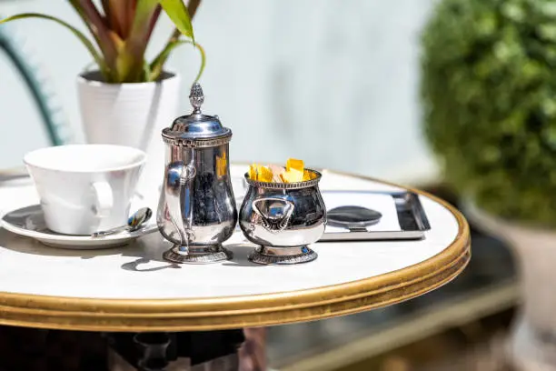 Closeup of table with used coffee or afternoon tea cup in outdoor outside cafe, nobody, stainless steel metal English teapot, sugar packets, spoon, plate in London, UK street
