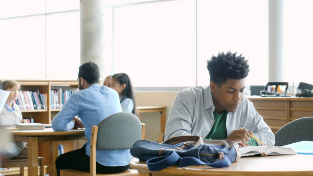 istock Teenage boy reads textbook in school library 994478728