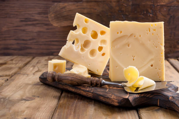 cheese with holes large and small. wooden board and knife. traditional dutch cheese. copy space - cheese emmental cheese switzerland grated imagens e fotografias de stock