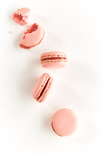 strawberry flavored macaroons in a white table and highlighted background, one with a bite