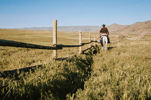 A rancher and his horse walk alongside a fence in rural Utah, USA.