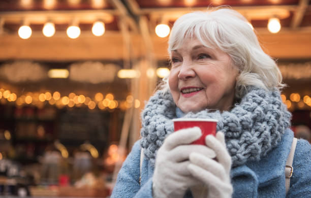 Happy mature lady warming up by hot beverage outdoor Enjoying winter holidays. Portrait of joyful senior woman drinking mulled wine with pleasure. She is standing on street and smiling. Copy space hot women working out pictures stock pictures, royalty-free photos & images