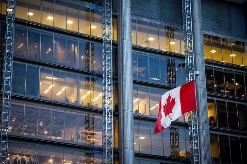 Picture of a flag of Canada waiving in the air in front of a business building in the city center of Toronto, the main city of Canada, and the economic and financial capital of the country.