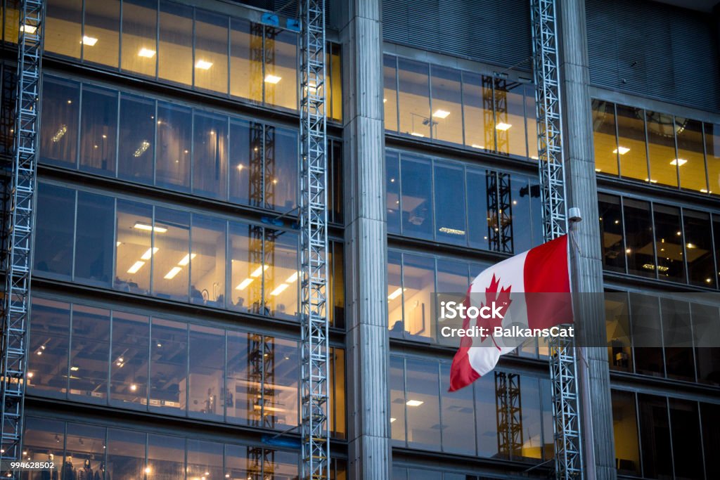 Canadian flag in front of a business building in Toronto, Ontario, Canada Picture of a flag of Canada waiving in the air in front of a business building in the city center of Toronto, the main city of Canada, and the economic and financial capital of the country. Canada Stock Photo