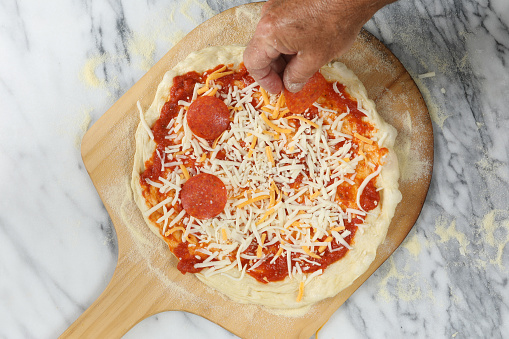 An overhead close up horizontal photograph of  chef's hand adding pepperoni to a pizza