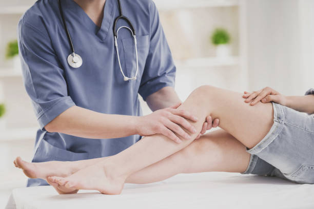 Close up. Doctor Comfforting Leg of Sitting Woman. Close up. Doctor in Blue Uniform Comfforting Leg of Sitting Young Woman in Doctor Office. Traumatology Medical Devices. Medical Treatment in Clinic and Healthcare Professional Concept. orthopedist stock pictures, royalty-free photos & images