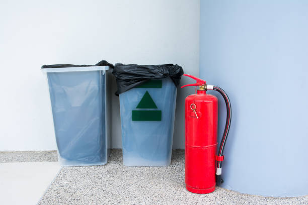 istock Fire extinguisher on floor beside plastic rubbish bin at building corner background 994659472
